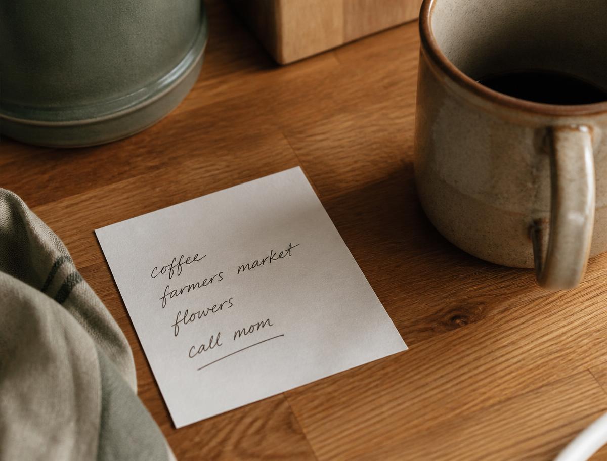 A handwritten note resting on a wooden counter beside a mug